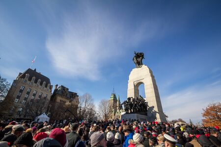 OTTAWA, CANADA - NOVEMBER 11, 2018: Crowd gathering on National War memorial, with parliament in background, on remembrance day to commemorate the canadians who died in conflictsPicture of a crowd gathering in front the National War Memorial of Ottawa oのeditorial素材