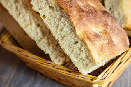Italian bread of Focaccia Genovese type on display on a basket on a rustic wooden table, sliced in...