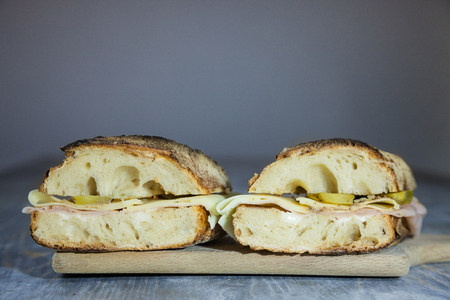 Ham and cheese sanwdich in a French baguette, made of Paris Ham and emmental with some sliced pickles, cut in two on display on a rustic wooden table.の写真素材