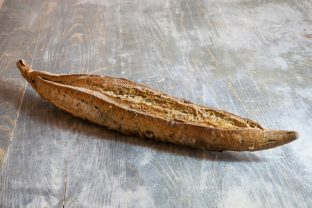 Traditional French baguette, a ficelle flute type, a thin version with seeds and grains, on display on a rustic wooden table.の写真素材