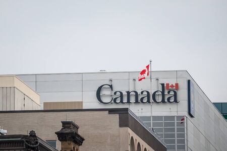 OTTAWA, CANADA - NOVEMBER 12, 2018: Canada Wordmark, the official logo of the Canadian government, on an administrative building next to a Canadian flag waivingPicture of the flag of Canada on a government building, with the official Canada Wordmark.  Eのeditorial素材