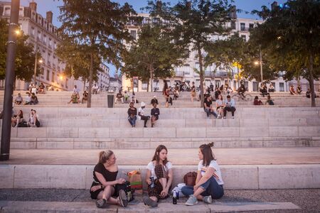 LYON, FRANCE - JULY 18, 2019: French people, mainly women and girls sitting on the riverbank of the Rhone (quais) in the evening while people are gathering for the tradition of aperoPicture of people sitting on the quays of the riverbank of the Rhone riのeditorial素材