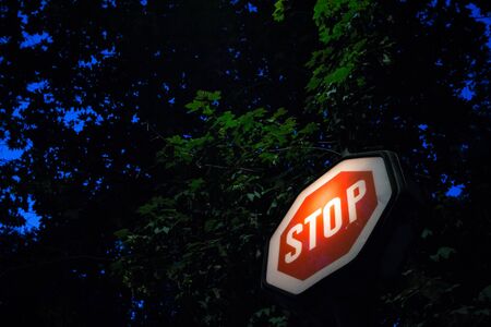 Old stop sign, obeying by european traffic regulations, lit during a dark night, indicating to all vehicles to stop and to yield to other cars

Picture of a typical stop sign, old design with its typical octagon shape, lit, during a dark evening. This stop road sign indicated to all vehicles to stop and let priority to cars passing byの写真素材