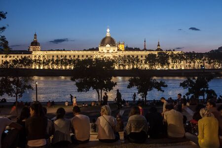 LYON, FRANCE - JULY 14, 2019: French people sitting on the riverbank of the Quais De Rhone, facing Hotel Dieu, one of the main monuments of the city for the tradition of apero

Picture of the Hotel Dieu at Dusk, with people sitting on the quays of the rivのeditorial素材
