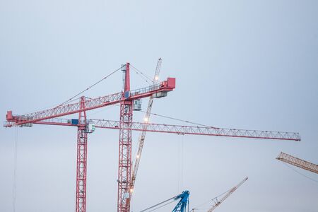 Group of cranes on a construction site, in front of a building being assembled taken from afar...