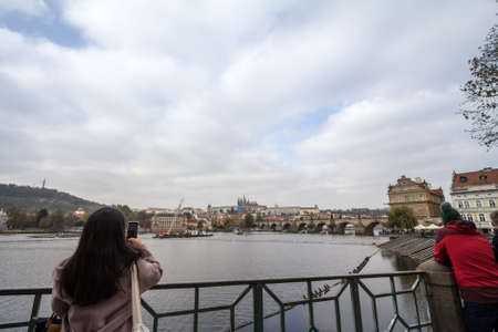 PRAGUE, CZECHIA - NOVEMBER 1, 2019: Tourist, a woman, taking a photo of the Vltava river and the...