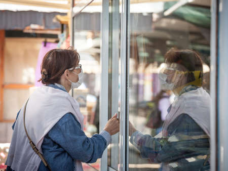 BELGRADE, SERBIA - APRIL 23, 2020: Old senior woman wearing a respiratory face mask looking at her reflection in a glass.のeditorial素材