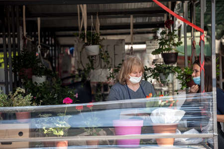 BELGRADE, SERBIA - APRIL 23, 2020: Woman a merchant on Belgrade green farmers market, selling plants and flowers wearing face mask protective equipment.のeditorial素材
