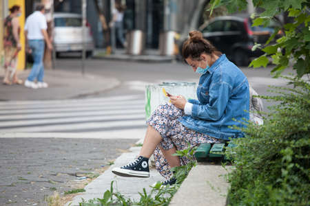 BELGRADE, SERBIA - JULY 13, 2020: Young woman wearing a respiratory face mask checking apps on her smartphone in the street of Belgrade.のeditorial素材