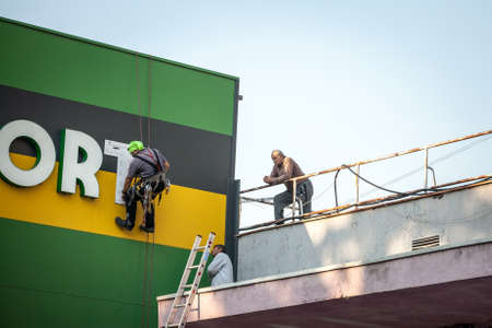 BELGRADE, SERBIA - OCTOBER 8, 2018: Three men, construction workers, wearing security equipment, fixing and renovating a building on a rooftop of an industrial facility.のeditorial素材
