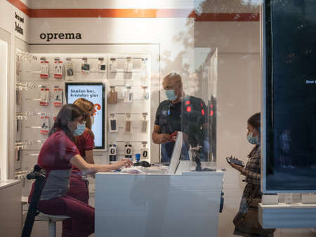 BELGRADE, SERBIA - JULY 28, 2020: Client disussing with a staff of a phone carrier shop wearing a respiratory face mask and checking apps smartphone in Belgrade.のeditorial素材