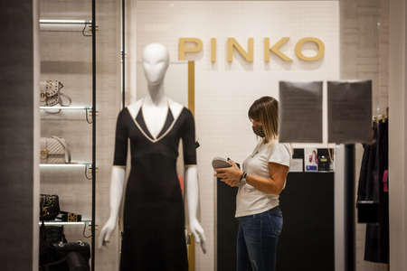 BELGRADE, SERBIA - SEPTEMBER 16, 2020: Employee of a fashion clothing boutique sitting alone around dresses wearing a respiratory face mask in Belgrade.のeditorial素材