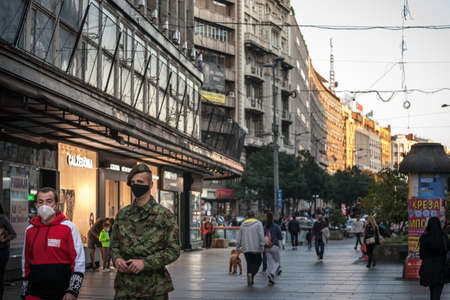 BELGRADE, SERBIA - OCTOBER 10, 2020: two men, including a soldier from the Serbian army in uniform walking in the streets of belgrade wearing face mask protective equipment.のeditorial素材