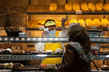 BELGRADE, SERBIA - OCTOBER 14, 2020: Female staff, Bakter, serving clients and holding cash banknotes in a bakery wearing a respiratory face mask in Belgrade.のeditorial素材