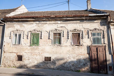Old windows and abandoned wooden door on the residential building of a farm in Vojvodina, Serbia, with a damaged and decaying facade.の写真素材