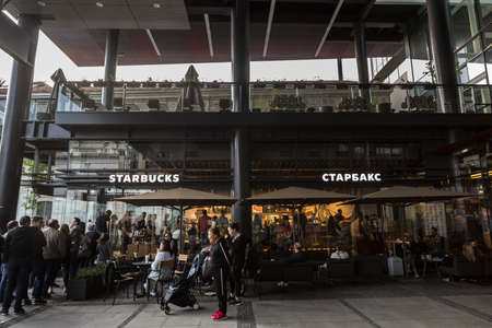 BELGRADE, SERBIA - APRIL 28, 2019: People queuing in front of a Starbucks logo on their main fast food with the name starbucks written in cyrillic and a crowd of clients queing waiting to buy their coffee. Picture of a Starbucks coffeehouse with a focus oのeditorial素材