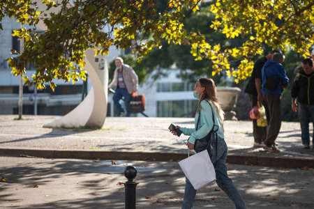 BELGRADE, SERBIA - OCTOBER 10, 2020: Young woman wearing a respiratory face mask rushing walking holding shopping bags in the street of Belgrade.のeditorial素材