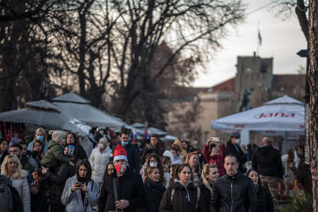 BELGRADE, SERBIA - JANUARY 1, 2021: Young man wearing a face mask with a christmas hat in a crowded Kalemegdan park.のeditorial素材