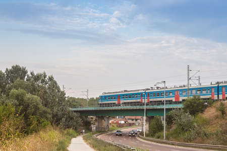 BELGRADE, SERBIA - AUGUST 25, 2019: Electric suburban train, an EMU of Beovoz BG Voz service, passing with a speed blur over a bridge with cars driving on a highway road in an interchange in Krnjaca most. Picture of a beovoz service train passing by a briのeditorial素材
