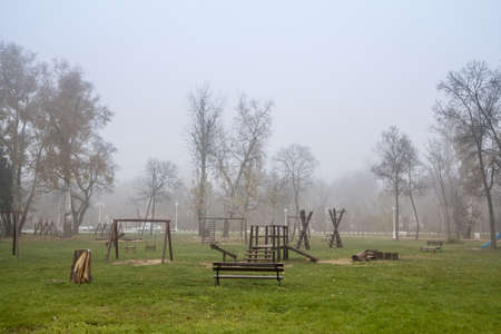Wooden children playground, a play area made of slides and swings, empty, in a mysterious foggy misty smog, during a cold winter or fall afternoon.の写真素材