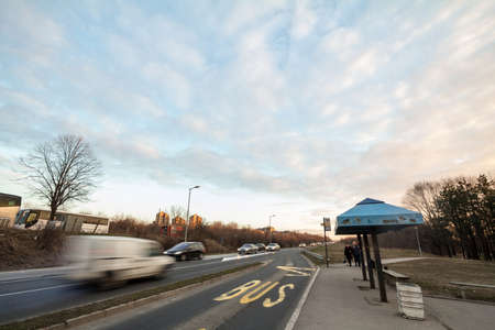 BELGRADE, SERBIA - MARCH 3, 2019: People waiting for a bus in the bus stop of Vidikovac while cars are driving fast with speed blur. It's a stop of Belgrade GSP, the public transportation system of the city. picture of a group of people waiting for a bus のeditorial素材