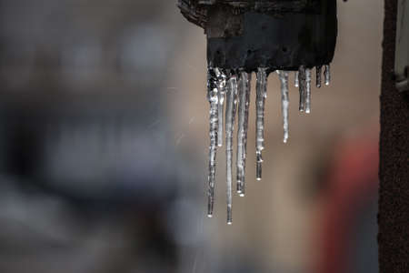 Icicles forming ice stalactites falling fron the edge of the eaves of gutters with droplets dripping in a residential building during a cold winter afternoon after a wave of snow made the temperatures falling.の写真素材