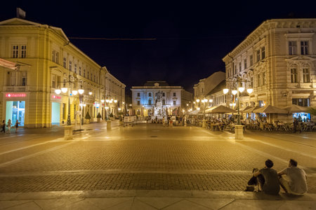 SZEGED, HUNGARY - JULY 20, 2017: Selective blur people standing on the deserted Klauzal ter square near Kossuth Lajos Statue in the city center of Szeged at night.のeditorial素材
