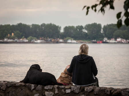 BELGRADE, SERBIA - JULY 26, 2020: Woman, alone, sitting outside with her two dogs, laying down near the Danube river in Zemun, during a break in a dog walking expedition.のeditorial素材
