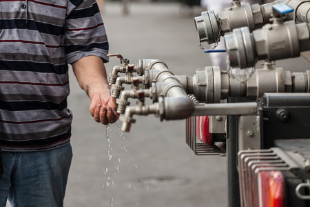 Water tap made of several pipes, with hands trying to hold water to save it and drink it. This faucet distributes to public a clean drinking waterの写真素材