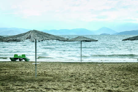 Panorama of a beach with parasol sun umbrella during a cloudy rainy afternoon on the Prespa lake on North Macedonian side. Prespa, or Prespansko ezero, is a Balkans lake between Macedonia, Greece and Albania.の写真素材