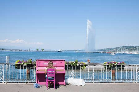 GENEVA, SWITZERLAND - JUNE 19, 2017: Female woman, amateur pianist, playing piano in front of Lake Geneva (Lac Leman) with its iconic Jet d'Eau (Water Jet), taken in a summer afternoon.のeditorial素材