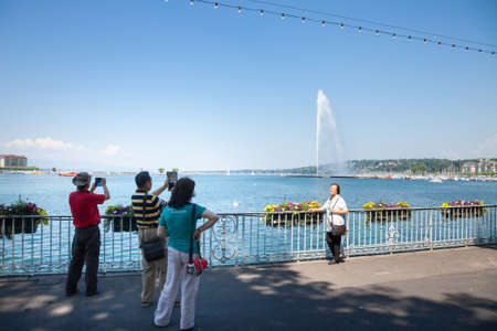GENEVA, SWITZERLAND - JUNE 19, 2017: Group of asian tourists from china taking pictures and smiling in front of Lake Geneva (Lac Leman) with its iconic Jet d'Eau (Water Jet), taken in a summer afternoon.のeditorial素材