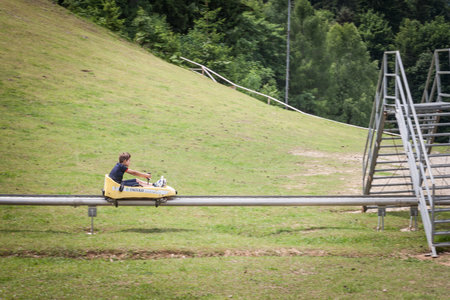 BLED, SLOVENIA - JUNE 12, 2021: Boy, a kid, going down a slope of Straza Bled with a bobsled on a...