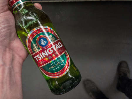 BELGRADE, SERBIA - JUNE 6, 2021: Hands holding a bottle of Tsingtao beer. Tsingtao Beer is a brand of Chinese lager beer produced in the Chinese city of Tsingtau.のeditorial素材