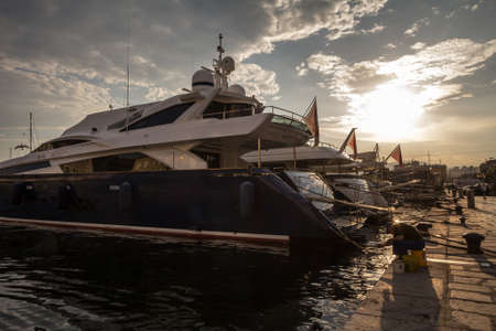 RIJEKA, CROATIA - JUNE 17, 2021: Old fisherman fihsing on the quay of Rijeka waterfront in front of a luxurious yacht ship boat anchored for fortuned people to spend the night on the marina.のeditorial素材