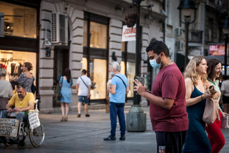 BELGRADE, SERBIA - AUGUST 4, 2021: Indian tourist, young man from india, shooting, filming & taking photos with smartphone in a belgrade street while traveling, wearing a facemaskのeditorial素材