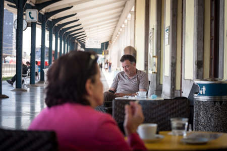 LJUBLJANA, SLOVENIA - JUNE 16, 2021: Selective blur on Man, old senior aged male, drinking coffee checking his smartphone at the terrace patio of a cafe  in the city center of Ljubljana.のeditorial素材