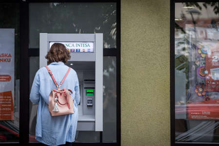BELGRADE, SERBIA - MAY 29, 2021: Young woman at a Banca Intesa ATM Bankomat withdrawing cash money in the city center of belgrade, the main hub of the Serbian Economy.のeditorial素材