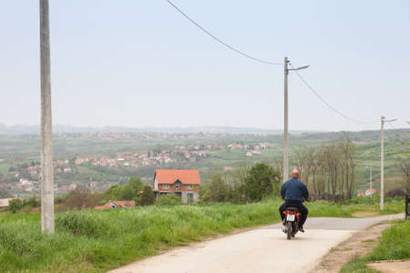 RIPANJ, SERBIA - MAY 1, 2021: Old senior man riding a motorcycle moped, biking on the rural countryside roads of Ripanj, in the agricultural part of serbia, plagued with demographic decline.のeditorial素材