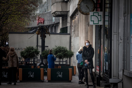 BELGRADE, SERBIA - APRIL 3, 2021: Young woman standing and waiting in front of a pharmacy wearing face mask protective equipment on Coronavirus Covid 19 crisis.のeditorial素材