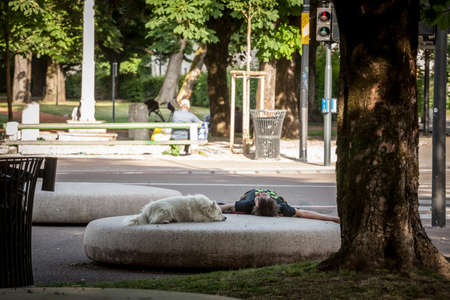 LJUBLJANA, SLOVENIA - JUNE 15, 2021: Selective blur on a middle adged man lying down, sleeping in a park of Ljubljana, having a nap with his pet, a dog.のeditorial素材
