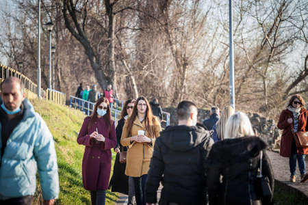 BELGRADE, SERBIA - MARCH 13, 2021: Two young Women, friends, walking in the middle of a crowd, one wearing face mask respiration protective equipement on Coronavirus Covid 19 crisis.のeditorial素材