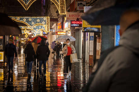 BELGRADE, SERBIA - DECEMBER 11, 2021: Selective blur on a young Woman wearing a respiratory face mask walking with her umbrella under heavy rain in a street of Belgrade, on coronavirus covid 19.のeditorial素材