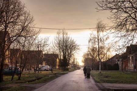 BANATSKO NOVO SELO, SERBIA - DECEMBER 19, 2021: Selective blur on a Serbian family, father, mother and a child, baby, in a stroller, walking in a countryside village of Vojvodina.のeditorial素材