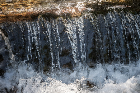 Streaming water, flowing through the rocks of a mountain alpine stream brook, with a speed blur on the water gurgling due to the movement of the flow.の写真素材