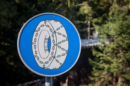 Close up on a european stand roadsign indicating snow chain wheels are mandatory in winter, to drive in ice, with its distinctive tire with snow wheels blue circle shape.の写真素材