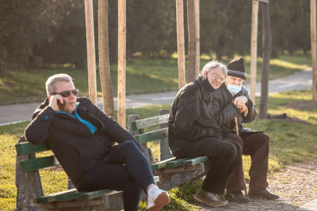 BELGRADE, SERBIA - MARCH 13 2021: Old men friends, sitting and discussing, smiling, happy, wearing facemask protective equipment under the nose on Coronavirus Covid 19 crisis.のeditorial素材