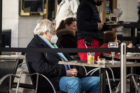 ARCACHON, FRANCE - FEBRUARY 22, 2022: Old senior man wearing a respiratory face mask sitting at the terrace of a cafe in Arcachon, relaxed and enjoying, during the coronavirus covid 19 health crisis.のeditorial素材