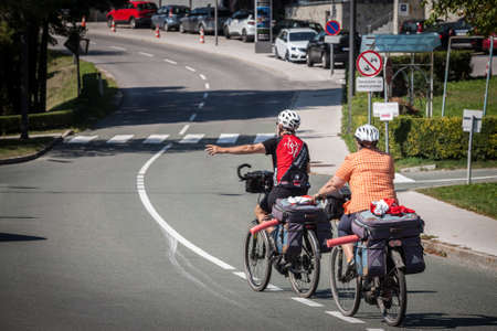 BLED, SLOVENIA - SEPTEMBER 11, 2021: Selective blur on a senior couple riding bicycle doing bike touring in bled, in the alps, with luggage on the bicycle, during a summer tourism travel.のeditorial素材