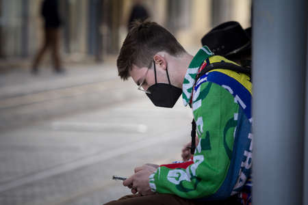 BORDEAUX, FRANCE - FEBRUARY 19, 2022: Young man, French wearing a respiratory face mask checking apps on his smartphone in the street of Bordeauxのeditorial素材